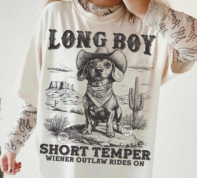 May include: A white t-shirt with a black and white illustration of a dachshund wearing a cowboy hat and bandana. The text "Long Boy Short Temper Wiener Outlaw Rides On" is printed on the shirt.