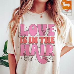 May include: A white t-shirt with a pink and red graphic that says "Love is in the hair" with butterflies around the text.