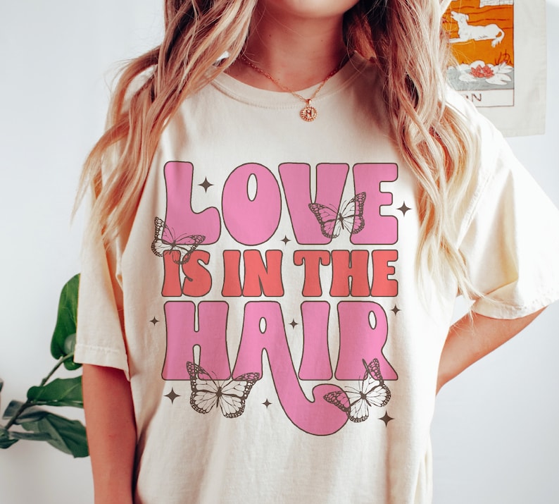 May include: A white t-shirt with a pink and red graphic that says "Love is in the hair" with butterflies around the text.