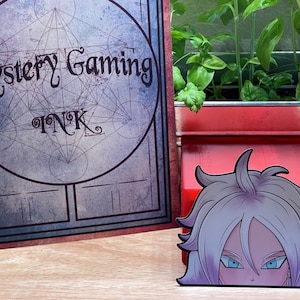 May include: A white and purple anime character with blue eyes peeking over the top of a red box. The box is labeled "Mystery Gaming Ink".