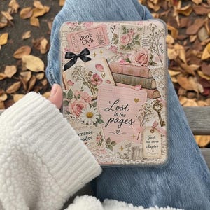 Peut inclure: Une coque de liseuse transparente avec un collage de roses roses, de livres empilés, d'un nœud noir, d'une clé dorée et de textes comme Book Club, Lost in the pages et Just one more chapter. Le design intègre des éléments en papier vintage et de la dentelle.