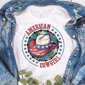 May include: White t-shirt with a red, white, and blue cowboy hat graphic. The graphic has a circle of stars around it and the text "AMERICAN COWGIRL".