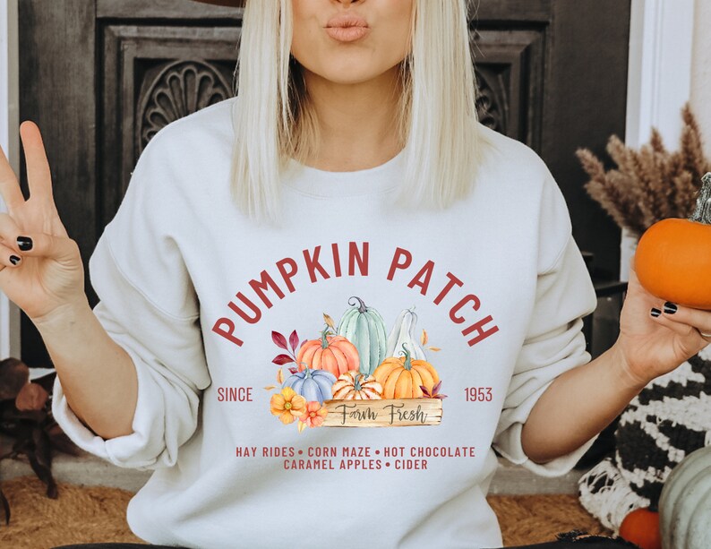 May include: Cream-colored sweatshirt with a "Pumpkin Patch" graphic. The design includes colorful pumpkins, leaves, and the text "Farm Fresh" and "Since 1953". Additional text includes "Hay Rides, Corn Maze, Hot Chocolate, Caramel Apples, Cider".