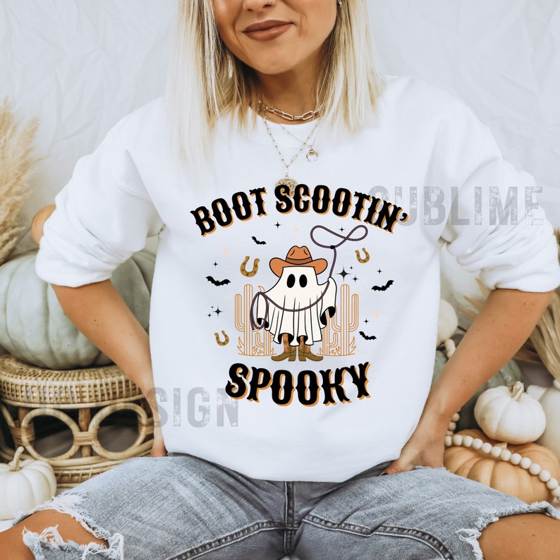 May include: White sweatshirt with a ghost wearing a cowboy hat and holding a lasso. The text "Boot Scootin' Spooky" is printed on the shirt.