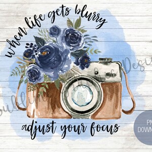 以下が含まれることがあります： 青い花と「when life gets blurry adjust your focus」というテキストが書かれた、ビンテージカメラの水彩画イラストです。