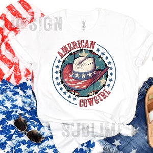 May include: White t-shirt with a red, white, and blue graphic of a cowboy hat with stars and the text "American Cowgirl".