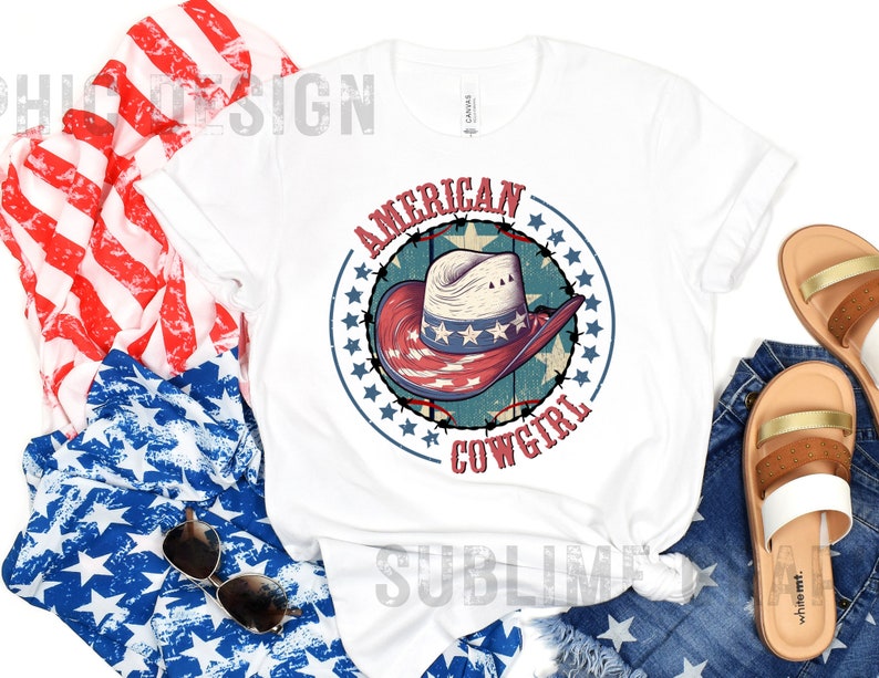 May include: White t-shirt with a red, white, and blue graphic of a cowboy hat with stars and the text "American Cowgirl".