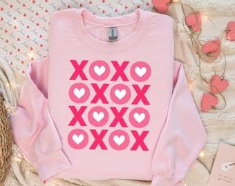 May include: Pink sweatshirt with a graphic design of repeated XOXO with hearts in pink and white.