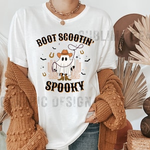 May include: White t-shirt with a ghost wearing a cowboy hat and lassoing a horseshoe. The text "Boot Scootin' Spooky" is printed on the shirt.