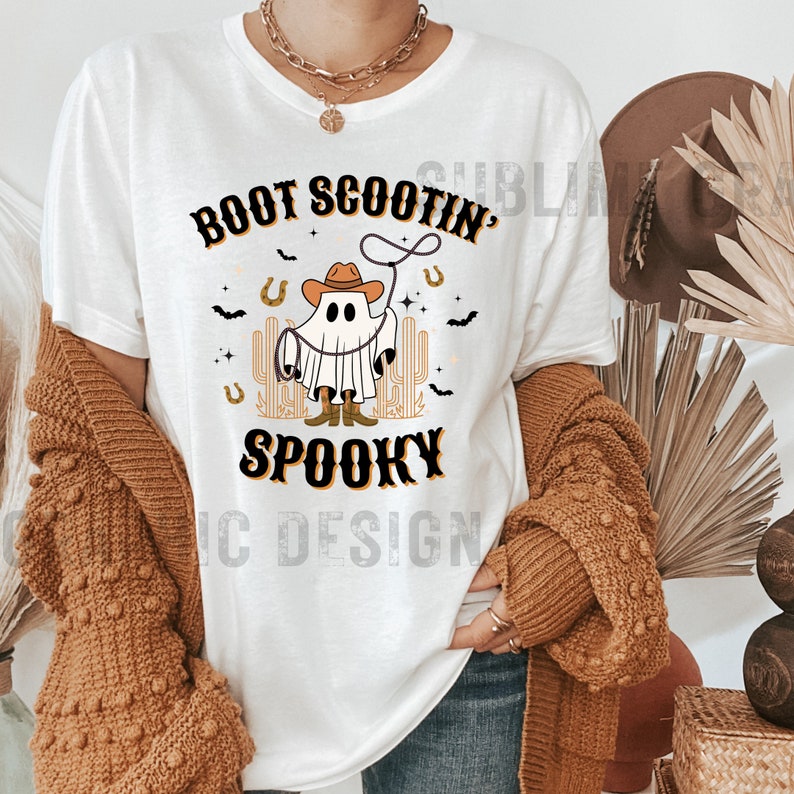 May include: White t-shirt with a ghost wearing a cowboy hat and lassoing a horseshoe. The text "Boot Scootin' Spooky" is printed on the shirt.