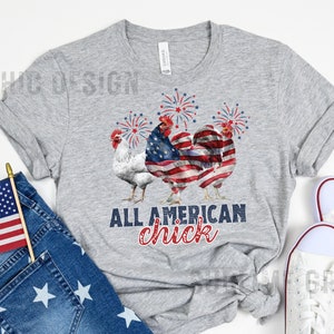 May include: A heather gray t-shirt featuring a graphic of three roosters with fireworks. The center rooster is designed with an American flag pattern. The text "ALL AMERICAN chick" is printed below the roosters in navy and red.