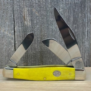 May include: A yellow handled pocket knife with three blades. The knife is open and the blades are visible. The knife has the words "Made in USA" on the side of the handle.
