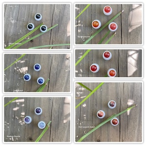 May include: Assortment of gemstone cabochons in various colours, including black obsidian, red aventurine, lapis lazuli, rainbow fluorite, and red leopard jasper. Each cabochon is set in a white metal bezel and displayed on a wooden surface.