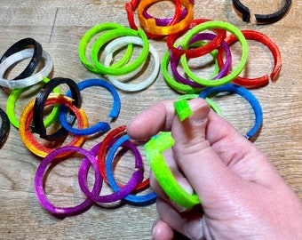 May include: A collection of colorful plastic rings in various sizes and colors, including green, blue, red, orange, purple, black, and white. The rings are arranged in a random pattern on a wooden surface.