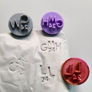 May include: Five different round rubber stamps with various letters and numbers. The stamps are in different colors, including gray, purple, and pink.