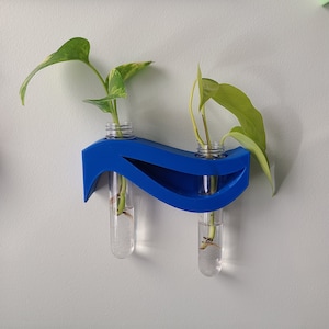 May include: A blue wall-mounted planter with two clear glass test tubes holding small potted plants. The planter is shaped like a wave and has a modern design.