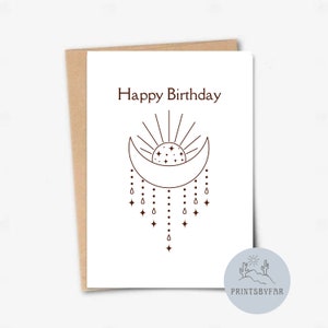 May include: A white greeting card with the words "Happy Birthday" in a dark brown font. The card features a crescent moon, sun, and star design with hanging star and teardrop accents. The card is inside a brown envelope.