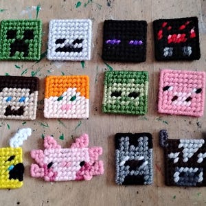 Peut inclure: Une collection de carrés en crochet représentant des personnages de Minecraft. Les motifs incluent un creeper vert, un zombie blanc, un enderman, une araignée rouge, Steve, Alex, un zombie, un cochon, une abeille, un axolotl, un loup et une vache.