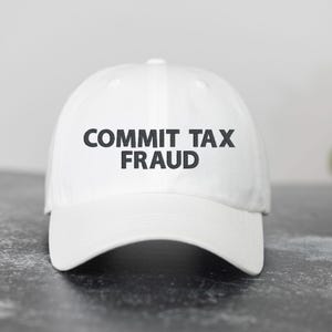 May include: White baseball cap with black text that reads "COMMIT TAX FRAUD".