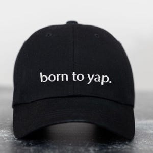 May include: Black baseball cap with white embroidered text that reads "born to yap."
