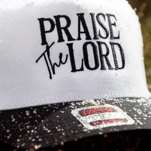 May include: White trucker hat with a black brim and black embroidered text that reads "PRAISE the LORD".