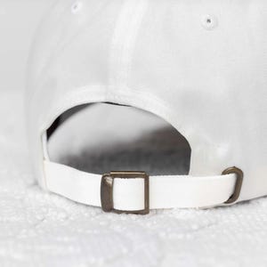 May include: White baseball cap with an adjustable strap and a brass buckle.
