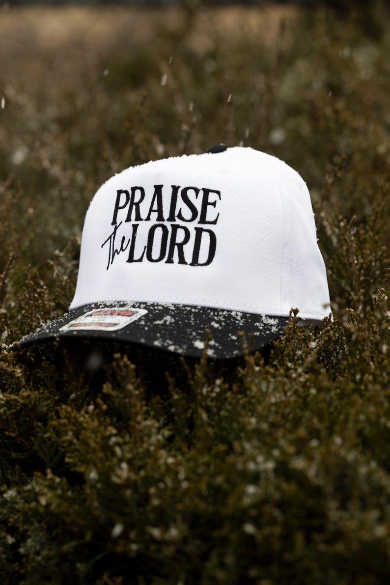 May include: A white and black baseball cap with the text "Praise the Lord" embroidered in black on the front.