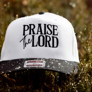 May include: White baseball cap with a black brim and black embroidered text that reads "Praise the Lord".
