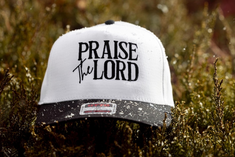 May include: White baseball cap with a black brim and black embroidered text that reads "Praise the Lord".