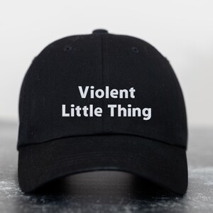 Op de afbeelding: Zwarte baseballpet met witte tekst die "Violent Little Thing" zegt.
