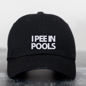 Puede incluir: Una gorra de béisbol negra con texto bordado en blanco que dice "I PEE IN POOLS".