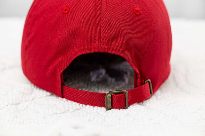 May include: Red baseball cap with a brown adjustable strap and buckle. The cap is made of a soft, cotton fabric.