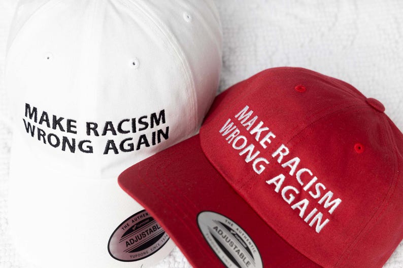 May include: Two baseball caps, one white and one red, both with the text "Make Racism Wrong Again" embroidered in black and white respectively.