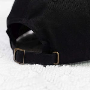 May include: Black baseball cap with a brown adjustable strap and buckle closure.
