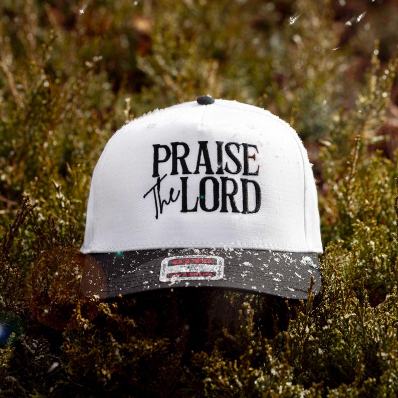 May include: White baseball cap with a black brim. The front of the cap has black embroidered text that reads "Praise the Lord".