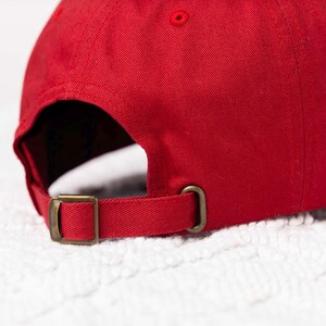 May include: A red baseball cap with a brown adjustable strap. The cap is made of a soft, cotton fabric.