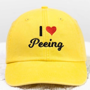 May include: A yellow baseball cap with a black embroidered heart and the text "I love Peeking" in black.
