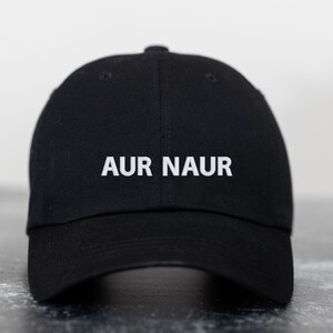 May include: A black baseball cap with white embroidered text that reads "AUR NAUR".