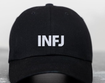 May include: Black baseball cap with the embroidered letters "INFJ" in white. The cap has a curved brim and a button on top. The hat is made of a soft fabric.