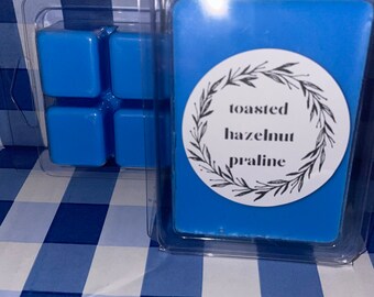 May include: A blue wax melt in a clear plastic container with a label that reads "toasted hazelnut praline".