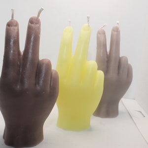 Könnte beinhalten: Drei handförmige Kerzen, eine braune, eine gelbe und eine hellbraune, jede mit zwei erhobenen Fingern in einem Friedenszeichen.
