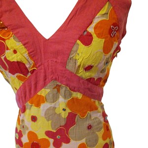 Puede incluir: Vestido sin mangas con escote en V y estampado floral. El vestido presenta un corpi&ntilde;o rosa y una falda con grandes flores en amarillo, naranja y rojo. Las flores est&aacute;n contorneadas en dorado y tienen detalles de lentejuelas.