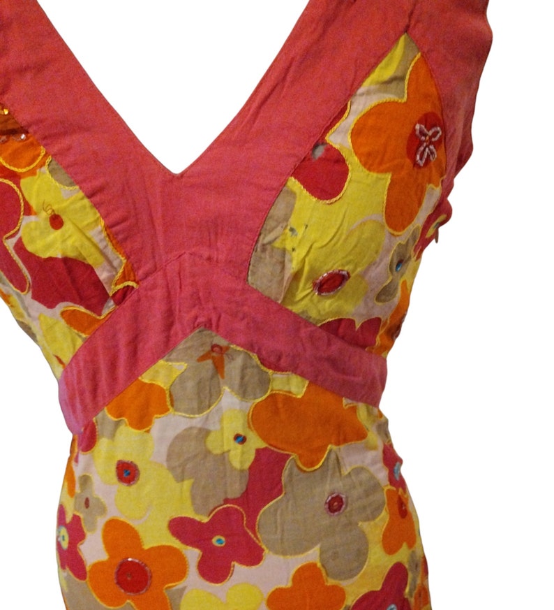 Puede incluir: Vestido sin mangas con escote en V y estampado floral. El vestido presenta un corpi&ntilde;o rosa y una falda con grandes flores en amarillo, naranja y rojo. Las flores est&aacute;n contorneadas en dorado y tienen detalles de lentejuelas.
