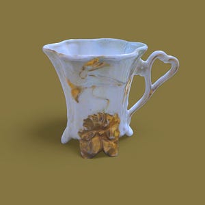 May include: A white porcelain teacup with a gold floral design and three gold feet. The cup has a handle in the shape of a loop.