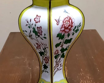 May include: A white and yellow cloisonné vase with a floral design. The vase has a square base and a round body. The flowers are pink, red, and green.