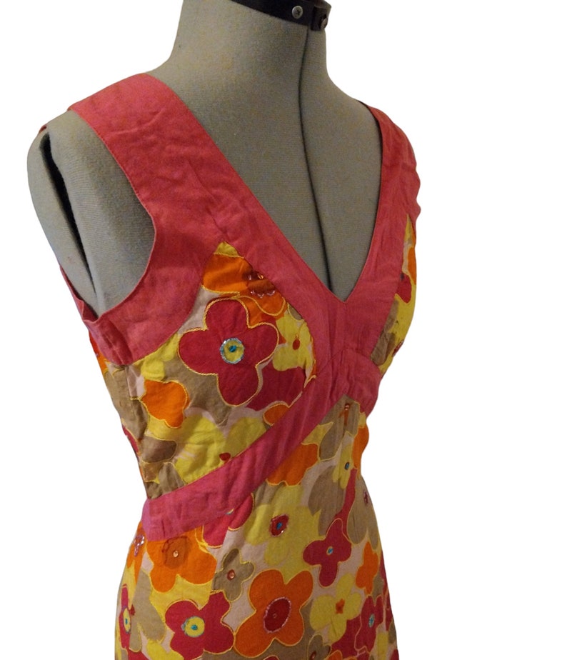 Puede incluir: Vestido sin mangas con escote en V, exhibido en un maniqu&iacute;. El vestido presenta un estampado floral en tonos rojos, naranjas, amarillos y marrones, con detalles en rosa. El vestido est&aacute; adornado con lentejuelas.