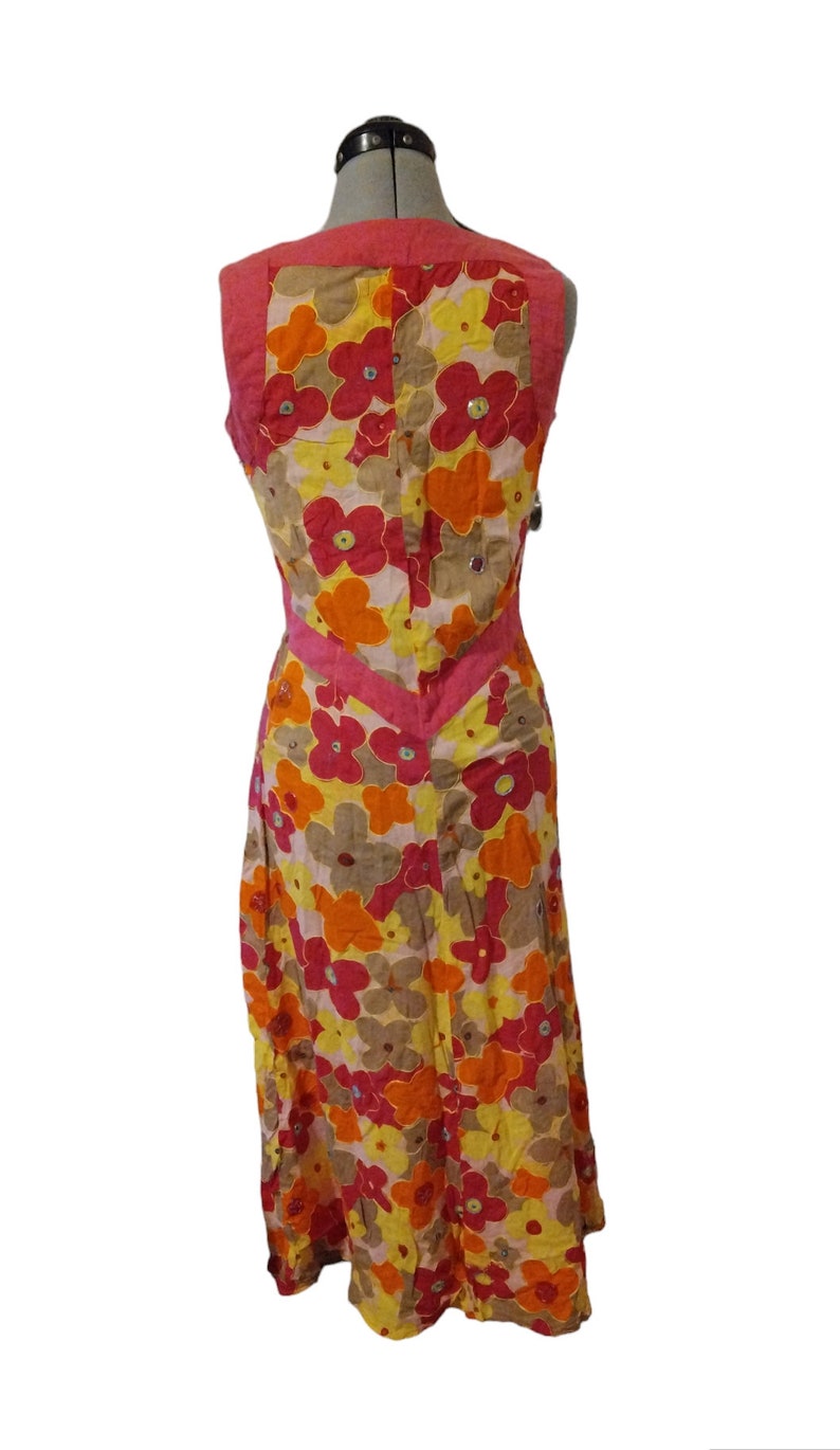 Puede incluir: Vestido sin mangas con estampado floral en tonos amarillos, naranjas y rosas. El vestido presenta un acento rosa en forma de V en la cintura y un panel rosa liso en los hombros. El vestido se exhibe en un maniqu&iacute;.