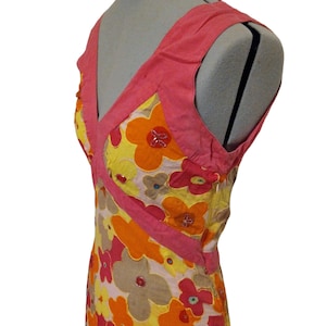 Puede incluir: Vestido sin mangas con escote en V, con un vibrante estampado floral. El vestido presenta una combinaci&oacute;n de flores amarillas, naranjas, rosas y marrones, con detalles de cuentas. El corpi&ntilde;o y las correas son de color rosa s&oacute;lido, creando un contraste llamativo.