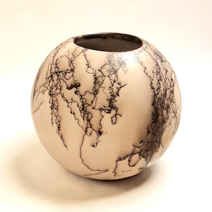 May include: A spherical ceramic vase with a smooth, matte off-white surface featuring intricate, dark black, branching, lightning-like patterns that wrap around the exterior. The vase has a circular opening at the top with a visible interior rim.