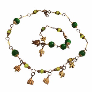 Könnte beinhalten: Ein grünes und goldenes Halsketten- und Armbandset mit Vogel- und Schildkrötenanhängern. Die Halskette hat mehrere Vogelanhänger, die daran baumeln.